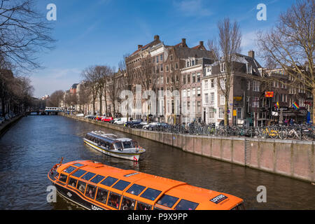 Dünne Grachtenhäuser und Sightseeing Boote auf touristische Kreuzfahrten auf einem Kanal in Amsterdam, Niederlande, Europa Stockfoto