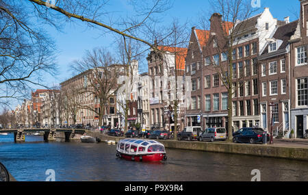 Amsterdam hohe enge Grachtenhäuser und ein touristisches Kreuzfahrtschiff auf einem Kanal, Niederlande, Europa Stockfoto