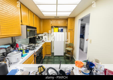 Unordentliche Wohnung Küche mit Eiche Schränke, Arbeitsplatten Fliesen, Gasherd, grüne Bodenbeläge und Stapel von Gerichten. Stockfoto