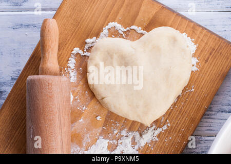 Teig für hausgemachte Kuchen, heart-shaped, auf einem Holzbrett und rollen Sie ein Handtuch mit einem Muster auf weißem Hintergrund. Freier Platz für Text oder Werbung. Stockfoto