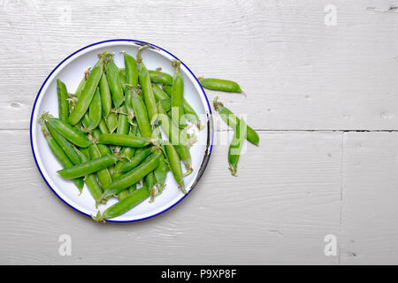 Pea pods in Weiß Metallschale auf lackierten Holz Küche Tisch Stockfoto