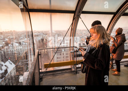 Touristen, die auf der Suche durch das Fenster im Blick auf Paris, Frankreich im Centre Georges Pompidou bei Sonnenuntergang Stockfoto