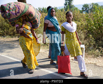 Indische lokale Frauen Ehefrauen der Landwirte, zu Fuß nach Hause nach dem Handel am lokalen Markt. Eine Frau trägt eine Matratze oder große Abdeckung auf dem Kopf. Stockfoto