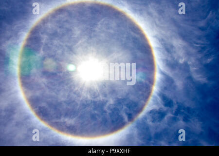 Solar Halo in einem sonnigen Sommer 12.00. Blauer Himmel mit weißen Wolken und ein Halo mit der Regenbogen Farben um die Sonne. Stockfoto