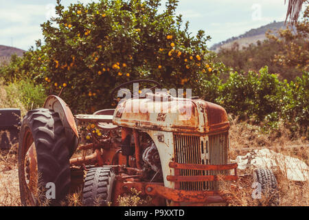 Einen alten verrosteten Traktor in einen orangefarbenen Feld. Stockfoto