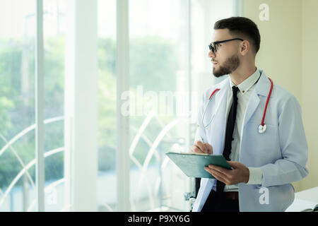 Glücklich lächelnde reife Arzt schriftlich über die Zwischenablage in ein modernes Krankenhaus. Kopieren Sie Platz. Stockfoto