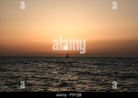 Segelboot oder Yacht vor der Küste Libyens mit metallisch spiegelnde Wasser im Vordergrund bei Sonnenuntergang Stockfoto