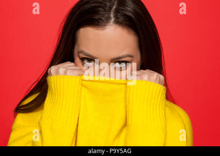 Schön schämen Frau in einem gelben Pullover auf rotem Hintergrund Stockfoto