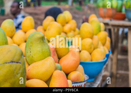 Gelbe, rote und grüne afrikanischen mango Obst in kleine Portionen für den Verkauf in einem Markt angeordnet. Stockfoto