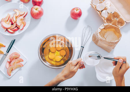 Die Frau Hände Messbecher aus Zucker mit den Eiern mischen Neben Zutaten zum Backen Apfelkuchen, Ansicht von oben. Weibliche Kochen Teig für Kuchen in der Nähe der Schnittlinie F Stockfoto