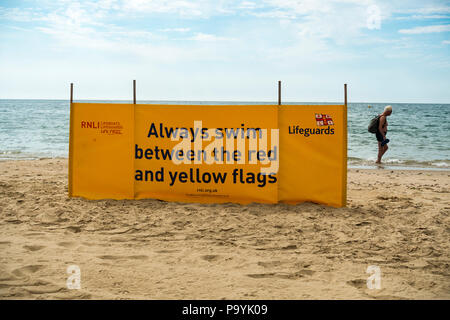 Warnhinweis am Strand zwischen dem roten und gelben Flaggen, um zu Schwimmen, mit einem Mann zu Fuß entlang der Küste, Strand von Bournemouth, Dorset, Großbritannien Stockfoto