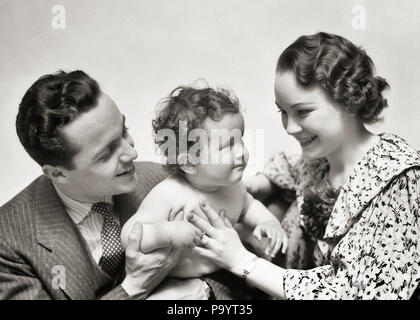 1940 PORTRAIT LÄCHELNDE MUTTER UND VATER HOLDING SÄUGLING SOHN-b 5886 HAR 001 HARS SCHÖNHEIT MÜTTER ALTE ZEIT NOSTALGIE UMARMT ALTE MODE 1 JUVENILE STYLE TEAMARBEIT KIND UMARMEN SÖHNE GERNE FAMILIEN FREUDE LIFESTYLE FRAUEN IM STUDIO SHOT GESUNDHEIT HOME LEBEN MIT HALBER LÄNGE HUG DAMEN PERSONEN PFLEGE MÄNNER, DIE VÄTER B&W Anzug und Krawatte GLÜCK WELLNESS FRÖHLICH UND VATIS STOLZ LÄCHELT VERBINDUNG FREUDIGES Wachstum von Jungfischen Mitte - Mitte - erwachsenen Mann Mitte der erwachsenen Frau MAMMEN ZWEISAMKEIT SCHWARZ UND WEISS KAUKASISCHEN ETHNIE HAR 001 ALTMODISCH Stockfoto