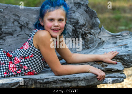 Atrtractive 8 jähriges Mädchen, in bunten jump Suit, die Haare hell blau gefärbt, an der Kamera auf der Suche und Festlegung auf der Werkbank. Model Release #113 Stockfoto