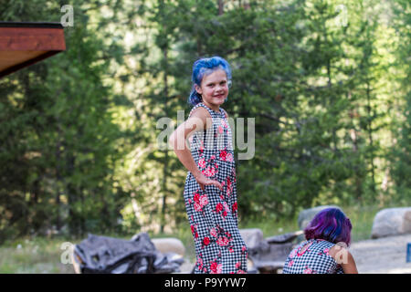 Atrtractive 8 jähriges Mädchen, in bunten jump Suit, die Haare hell blau gefärbt, an der Kamera und in den Bäumen. Model Release #113 Stockfoto