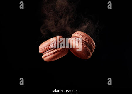 Französische Schokolade Macaron mit Kakaopulver auf schwarzem Hintergrund Stockfoto