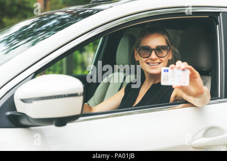 Glückliche junge Frau ihren Führerschein durch das Fenster Stockfoto