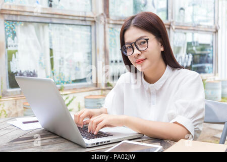 Junge asiatische Frau mit Brille arbeiten auf ihrem Computer im Freien in ihrem Garten, gut für modernen Lebensstil oder Menschen mit Technik Konzept Stockfoto