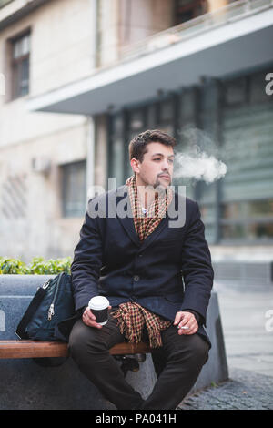 Gut aussehenden Mann Standortwahl auf der Werkbank auf Straße, rauchen Zigaretten und Kaffee. Stockfoto