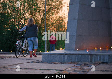 Frau mit Fahrrad Wandern im Park. Romantische Lagerfeuer Nacht am Meer bei Sonnenuntergang. Leute versammeln um Nacht der alten Leuchten feiern Stockfoto