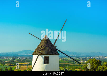 Schöne alte mittelalterliche White Wind Mühle im Tal mit grünen Vegetation Bäume Wiesen auf Berge und blauer Himmel. Traumhafte Landschaft Panorama Stockfoto