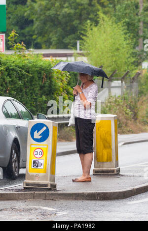 Ashford, Kent, Großbritannien. 20 Jul, 2018. UK Wetter: Met Office haben einen gelben Wetter Warnung für den Südosten mit starken Regenfällen. Eine Frau mit Regenschirm wartet auf eine Verkehrsinsel. © Paul Lawrenson 2018, Foto: Paul Lawrenson/Alamy leben Nachrichten Stockfoto