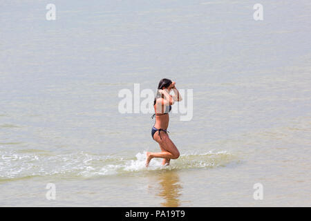 Bournemouth, Dorset, Großbritannien. Juli 2018 20. UK Wetter: heiß und feucht, mit trüben Sonnenschein in Bournemouth, als Sonnenanbeter Kopf ans Meer in Bournemouth Strand das schöne Wetter zu genießen. Junge Frau im Bikini läuft im Meer. Credit: Carolyn Jenkins/Alamy leben Nachrichten Stockfoto