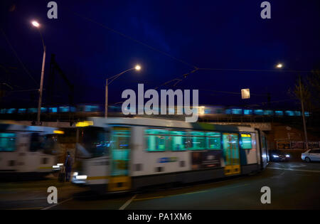 Ein Mann steht immer noch auf eine Straßenbahn als zwei strassenbahnen Pass in Richtung vor und hinter ihm. Ein Zug fährt auf der Brücke nur Overhead. Stockfoto