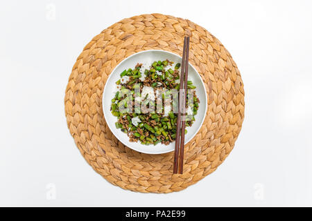 Schüssel mit Hackfleisch Eintopf mit Bohnen serviert über gekochten Reis mit Essstäbchen auf einem runden Strohmatte Stockfoto