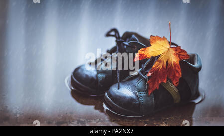 Nahaufnahme eines kleinen Baby Stiefel in der Pfütze mit trockenen Maple Leaf, Schuhe wasserdicht Kind, Herbst Jahreszeit Konzept Stockfoto