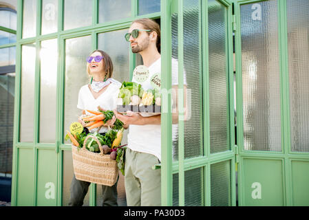 Junge vegetarische Paar aus dem Markt halten Beutel und Kasten voll kaufte gerade frische Produkte Stockfoto