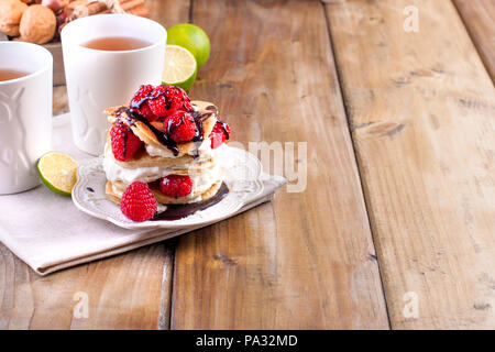 Sweet Home punkcakes mit weißer Sahne und frischen roten Beeren Himbeere. Zwei Gläser Tee zum Frühstück. auf einem hölzernen Hintergrund. freier Platz für Text oder Werbung Stockfoto