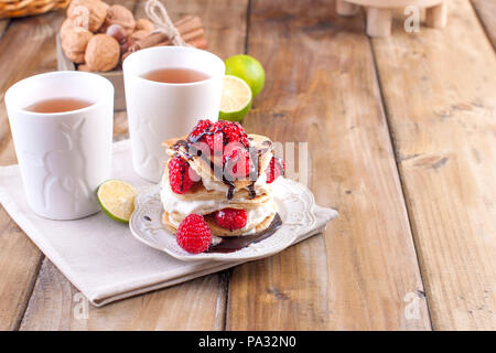 Sweet Home punkcakes mit weißer Sahne und frischen roten Beeren Himbeere. Zwei Gläser Tee zum Frühstück. auf einem hölzernen Hintergrund. freier Platz für Text oder Werbung. Stockfoto