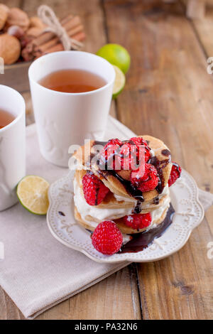 Sweet Home punkcakes mit weißer Sahne und frischen roten Beeren Himbeere. Zwei Gläser Tee zum Frühstück. auf einem hölzernen Hintergrund. freier Platz für Text oder Werbung. Stockfoto