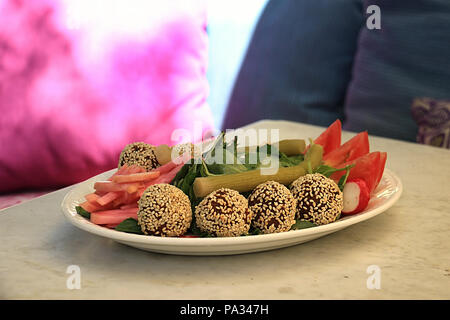 Falafelkugeln in Sesam in einer Schüssel zusammen mit der traditionellen begleitenden Gemüse abgedeckt. Stockfoto