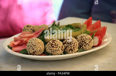 Falafelkugeln in Sesam in einer Schüssel zusammen mit der traditionellen begleitenden Gemüse abgedeckt. Stockfoto