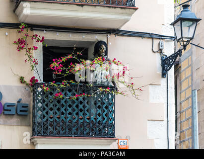 Mannequin in Kleidung und Gasmaske auf der gewöhnlichen Barcelona Balkon mit roten Blumen verdreht. Stockfoto