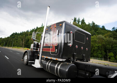 Schwarz klassische amerikanische Motorhaube leistungsstarke stilvolle Big Rig Semi Truck mit vertikalen Auspuffrohre und Chrom Akzent Teile auf der Kabine mit Schlafplatz für t Stockfoto