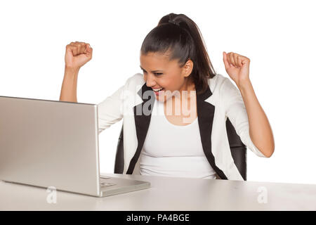 Glückliche junge geschäftsfrau mit einer gewinnenden Geste auf ihr Notebook suchen Stockfoto