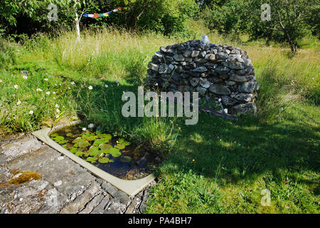 Ein wildlife Teich, Stein Pflaster & ein Cairn, gemacht mit einem recycelten Badewanne und Mauerwerk aus einer abgerissenen Verlängerung, in einem bewaldeten Garten in der Nähe von Caernarfon, Großbritannien. Stockfoto