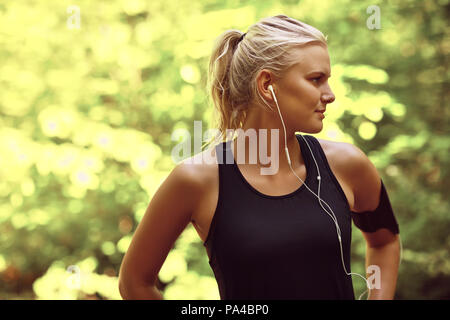 Passen junge blonde Frau in Sportkleidung Wiedergabe von Musik auf einem Handy in ein Armband, bevor Sie für einen Wald Stockfoto