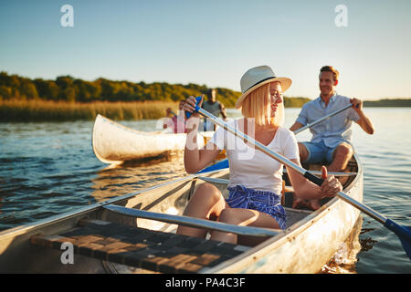 Junge Frau lachend, während ein Kanu paddeln auf einem See mit ihrem Freund und einem anderen Paar an einem sonnigen Nachmittag Stockfoto