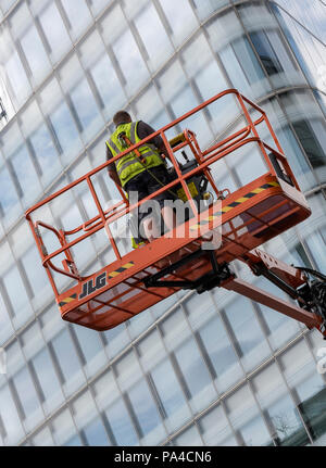 Ein Mann mit einem mobilen Hubsteiger oder mewp Cherry Picker Zugang zu einem hohen verglasten Bürogebäude in London zu gewinnen Stockfoto