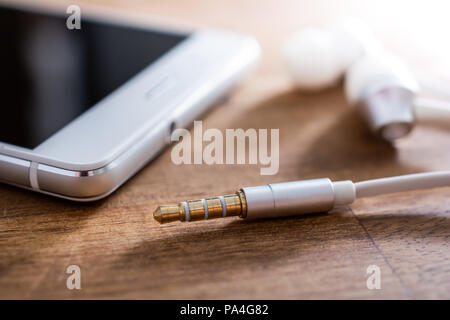 In-Ear Kopfhörer und Kabel liegen Neben einem weißen Mobiltelefon auf hölzernen Tisch Stockfoto