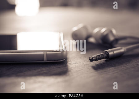 In-Ear Kopfhörer und Kabel liegen Neben einem weißen Handy in monochromen Farben Stockfoto