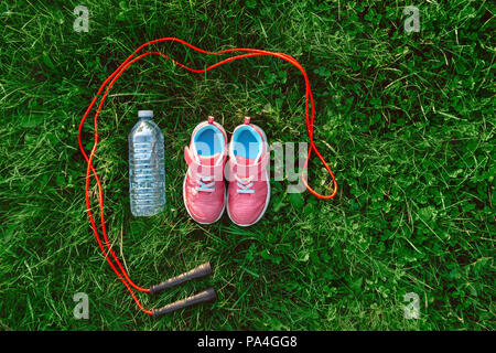 Flatlay mit Paar rosa Mädchen Sneaker Schuhe, Seil springen und eine Flasche Wasser im grünen Gras außen, Ansicht von oben. Aktivität Erholung Konzept. Stockfoto