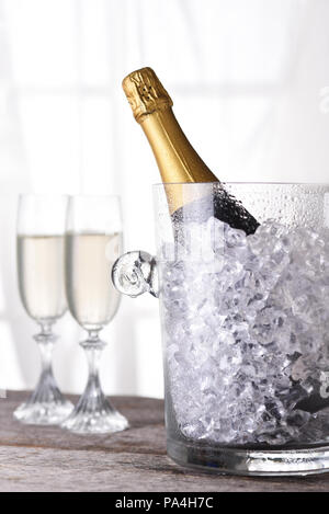 Eine Flasche Champagner in einem Eiskübel vor ein Fenster mit zwei Flöten im Hintergrund. Stockfoto