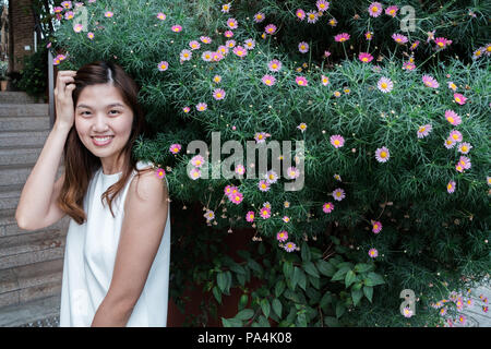 Porträt der Schönen und süßen asiatischen Mädchen Spaß mit Büschen von daisy flower als Hintergrund. Stockfoto