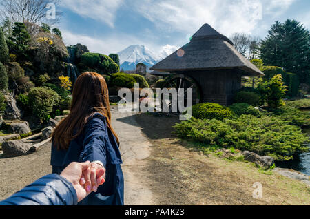 Portrait von schönen Frauen ihren Freund an der Hand halten und ihn in ein kleines Dorf mit Mount Fuji führenden im Hintergrund. Paar in der Liebe. Stockfoto