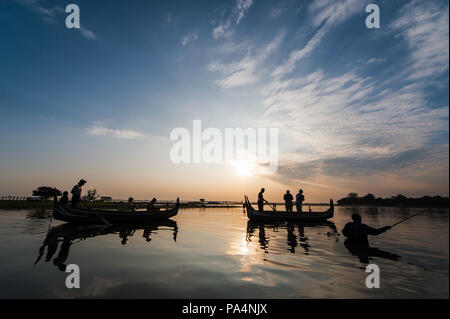 Boote mit Touristen auf dem Taung Tha Mann See mit der U-Bein Brücke im Hintergrund, während ein Sonnenuntergang in Mandalay, Myanmar Stockfoto