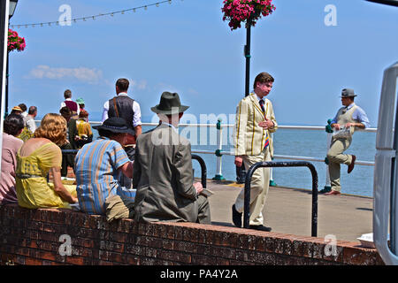 Mittagessen - Pause während der Dreharbeiten zu "sechs Minuten bis Mitternacht". Penarth Pier, S. Wales. Schöner Mann in hat lehnt sich lässig an Geländer auf der Promenade. Stockfoto